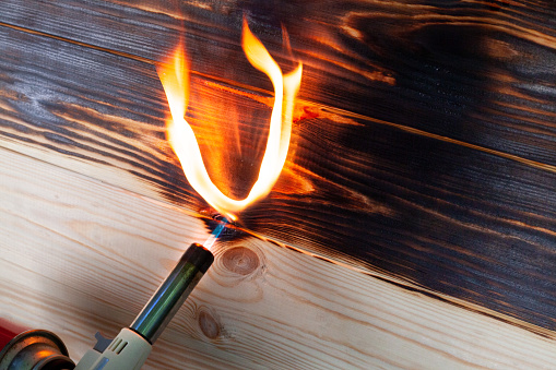 Burning wooden board by gas-burner. Brushing with a gas burner at home. Treating the soft part of wood with fire. Decoration of wooden products.