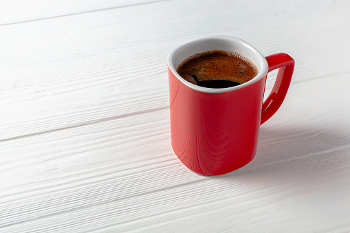 A red cup of strong coffee on white table. Red mug with coffee.