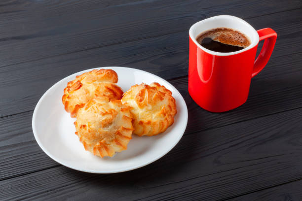 Golden profiteroles filled with cream, served with a cup of coffee on dark table. a delightful dessert pairing for any occasion