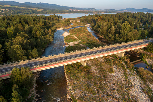 Aerial view of a three cyclists on a bridge over a river near a lake in a beautiful holiday region.