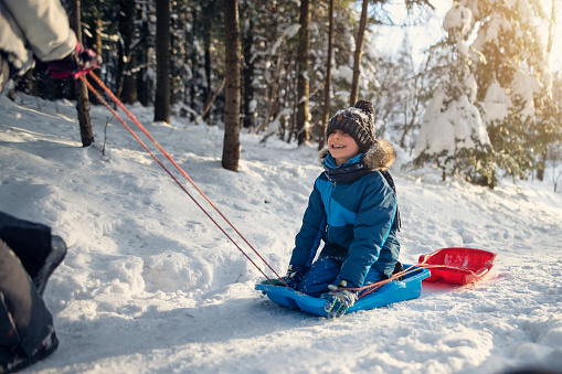 Teenage girl is pulling her laughing younger brother on a sled in the winter forest.
Shot with Nikon D850