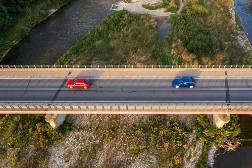 Aerial view of two cars driving on a bridge over a river near a lake in a holiday region.