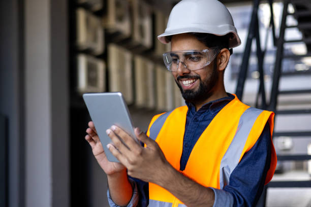 istock Portrait of young engineer worker, man in helmet and vest using tablet computer, smiling, checking production figures 1805603389