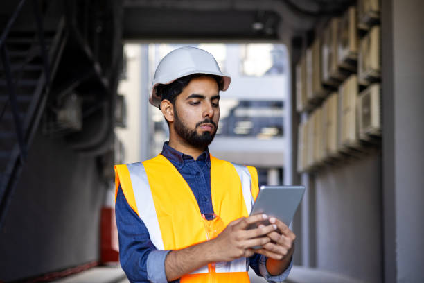 istock Serious thinking and focused engineer working in factory in hard hat and vest, man using tablet computer reading diagram, and checking equipment, inside industrial factory 1805603397