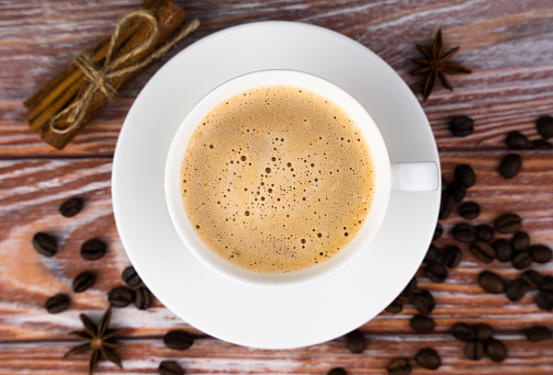 Cup of fresh coffee and scattered coffee beans on a wooden background. Preparation of natural coffee. Close-up. Top view. Selective focus.