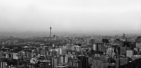 An aerial view of a bustling city skyline with a majestic mountain range in the background, captured in classic black and white
