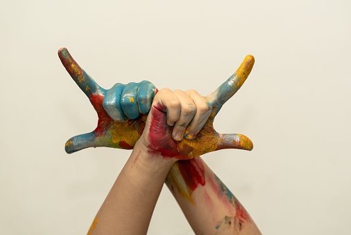 A closeup of a child's paint-covered crossed hands with fingers gesturing upwards.