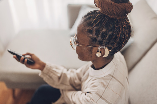 Young beautiful woman watching tv while wearing hearing aid at home