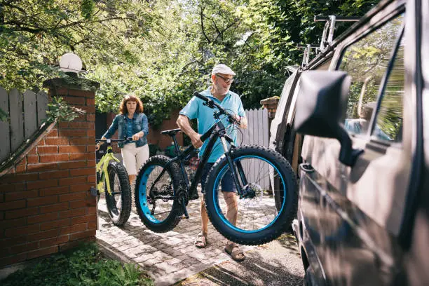 Senior couple, each with a fatbike in hand, strategically loads their bikes into the campervan, ready to roll into the next chapter of their journey together.