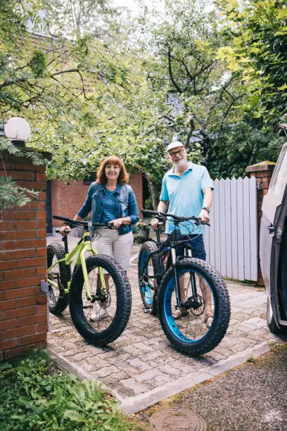 Senior couple, framed by the familiar surroundings of their driveway, poses with their fatbikes, showcasing the beauty of an active lifestyle