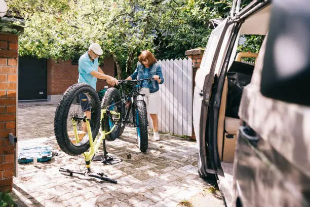 Active senior couple, checks the tires and gears of their fatbikes, preparing for an adventurous vacation with their trusty campervan parked near them.