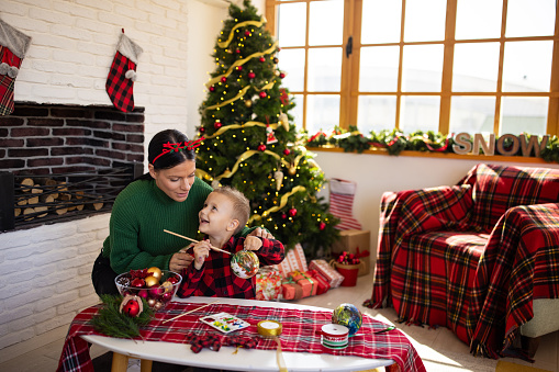 A mid adult Caucasian woman helping her son make a Christmas ornament in the living room of their apartment