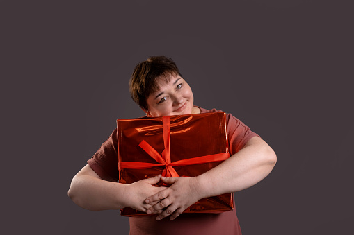 curvy woman hugging and holding gift box. happy to receive a Christmas present on neutral grey background