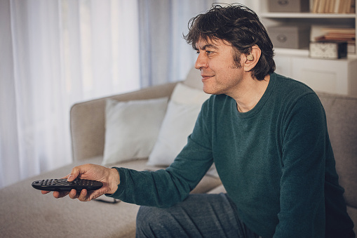 Middle aged man wearing hearing aid relaxing at home