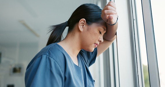 Healthcare nurse, stress and headache by window for working burnout, frustrated employee and tired asian woman in hospital. Doctor, pain and sad medical worker, anxiety or mental health depression