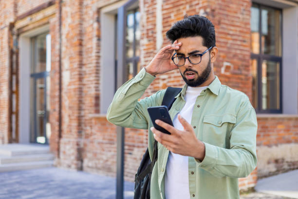 istock Upset and disappointed student with backpack outside university campus holding phone, reading bad news, man browsing social media, unhappy 1805645266