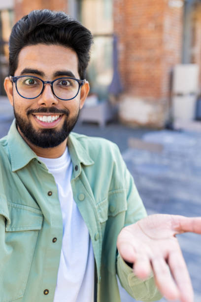 istock Phone web camera view, young man uses app on smartphone for remote video call communication, Indian man smiles and looks at camera, waves hand in greeting, Vertical shot 1805645271