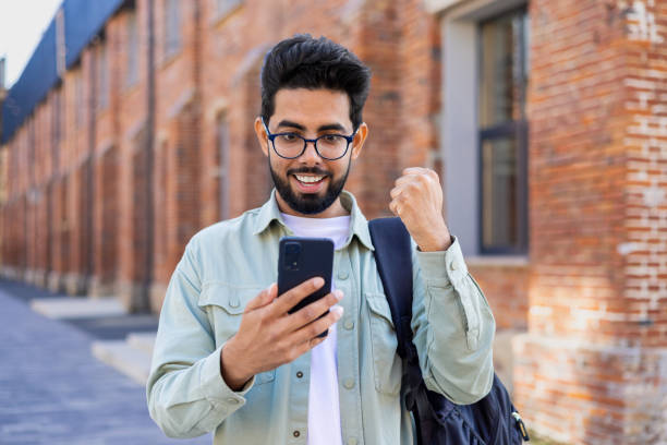 istock Young indian student received online win notification message phone, successful entrance exam results, man with backpack walking outside university campus, celebrating successful achievement result 1805645275
