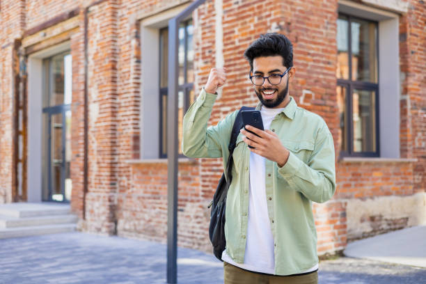istock Young indian student received online win notification message phone, successful entrance exam results, man with backpack walking outside university campus, celebrating successful achievement result 1805645276