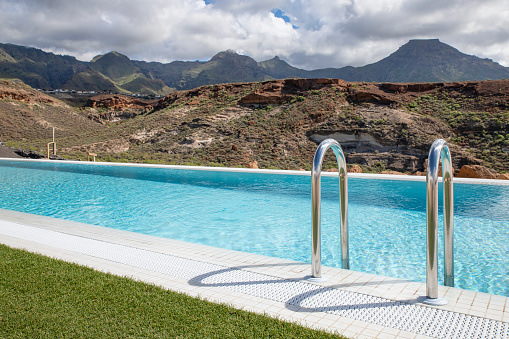 Views of a large luxurious swimming pool surrounded by the natural mountainous landscape, excellent environment for recreational activities and leisure, outdoors space as part of a property or a hotel.