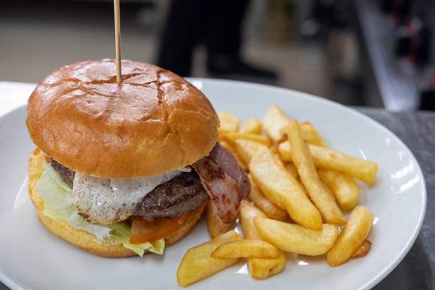 Large burger with egg and salad, and a big portion of fried chips aside set on a plate ready to be served Large burger with egg and salad, and a big portion of fried chips aside set on a plate ready to be served, meal preferred for its taste, convenience and variety, consumed in different social occasions. spanish hamburger stock pictures, royalty-free photos & images