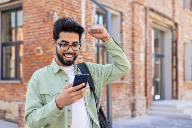 istock Young indian student received online win notification message phone, successful entrance exam results, man with backpack walking outside university campus, celebrating successful achievement result 1805649871
