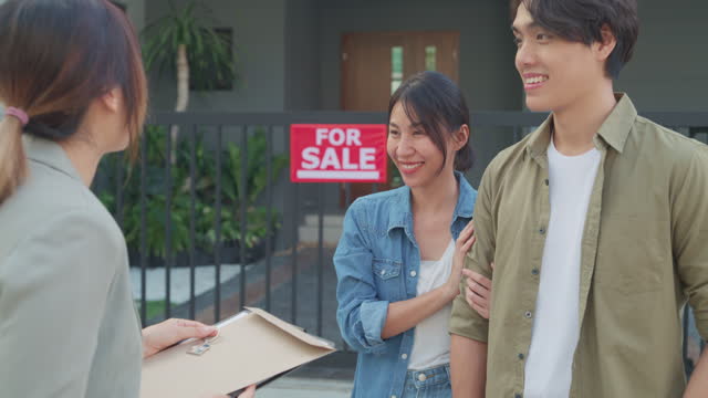 Closeup of young Asian woman real estate broker showing house to client buyers outside at home. Buying a new house.