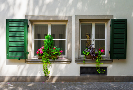 Zurich, Switzerland - June 18, 2023: Wooden window decorated with flowers. Typical facades of buildings in Zurich. Flowers under shuttered. A walk through the city on a sunny day