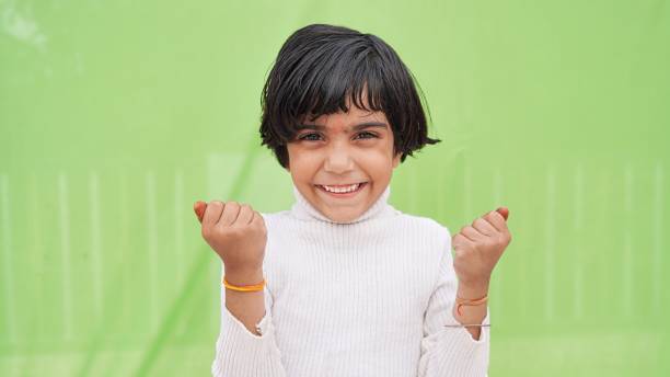 concepto de victoria. retrato de un niño asiático emocionado con las manos levantadas agitando los puños sobre el fondo verde - child asian and indian ethnicities facial expression asia fotografías e imágenes de stock