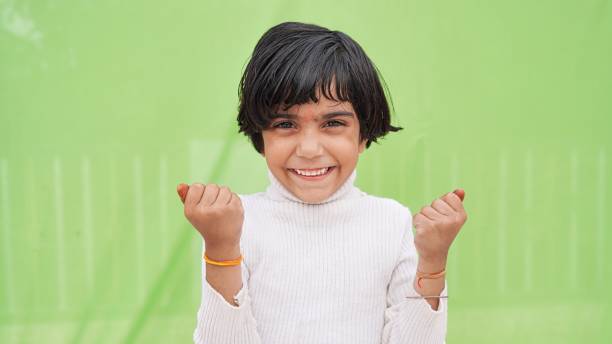concept gagnant. portrait d’un enfant asiatique excité avec des mains levées serrant les poings sur fond vert - child asian and indian ethnicities facial expression asia photos et images de collection