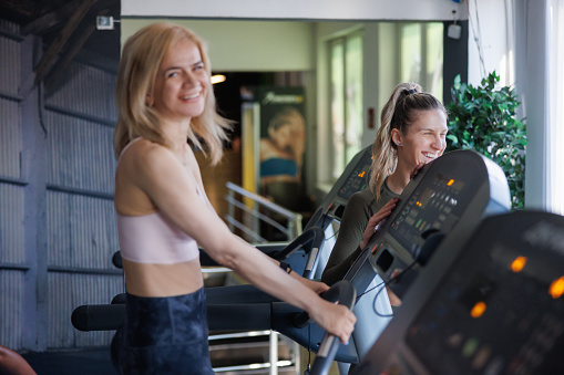 Happy mid adult woman working out on treadmill in the gym, female fitness instructor smiling
