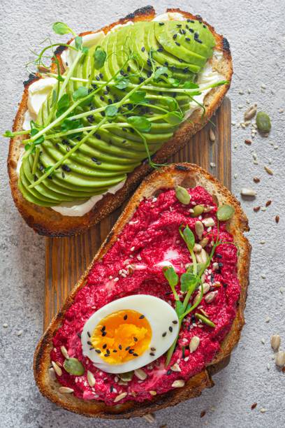 istock Whole grain toast with cream cheese, avocado, beetroot hummus, seeds, egg and microgreens (sprouted pea sprouts) on a light gray background. Healthy food concept. 1805703612