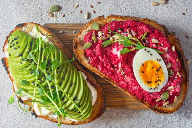istock Whole grain toast with cream cheese, avocado, beetroot hummus, seeds, egg and microgreens (sprouted pea sprouts) on a light gray background. Healthy food concept. 1805703614