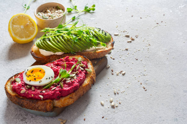 istock Whole grain toast with cream cheese, avocado, beetroot hummus, seeds, egg and microgreens (sprouted pea sprouts) on a light gray background. Healthy food concept. 1805703622
