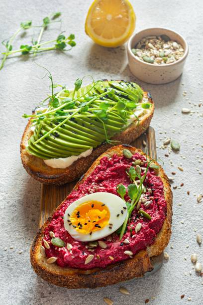 istock Whole grain toast with cream cheese, avocado, beetroot hummus, seeds, egg and microgreens (sprouted pea sprouts) on a light gray background. Healthy food concept. 1805703623