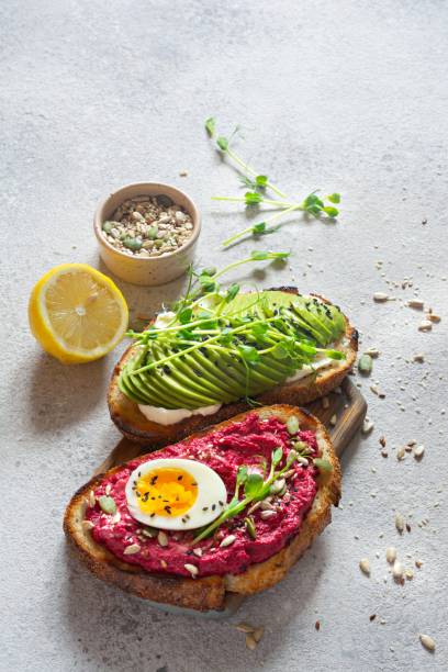 istock Whole grain toast with cream cheese, avocado, beetroot hummus, seeds, egg and microgreens (sprouted pea sprouts) on a light gray background. Healthy food concept. 1805703634