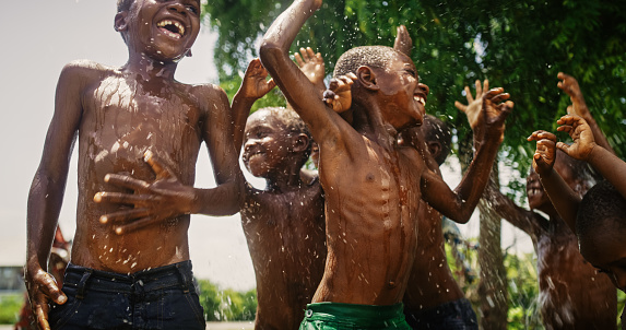 Group of African Kids Jumping and Laughing when Water Gets Poured on Them. Happy and Innocent Black Children Playing and Enjoying the Blessing of Rain Water After Long Drought