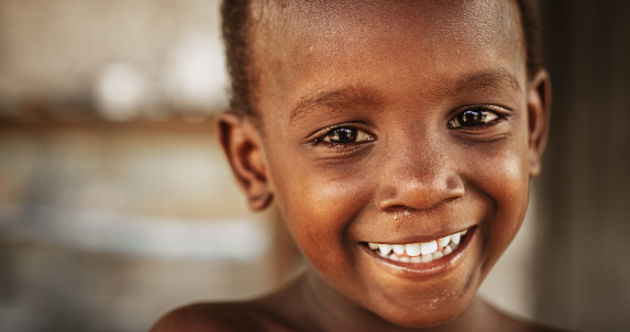 Close Up Portrait of a Shy Authentic African Boy Smiling and Laughing at the Camera with a Blurred Background. Black Male Kid Representing Future, Hope, and Acceptance. Documentary Footage