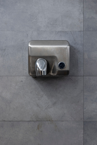 Detail of a hand dryer hanging on a gray tile wall. Front view. Copy space