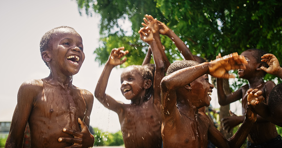 Group of Happy and Innocent Black Children Playing and Enjoying the Blessing of Rain Water After Long Drought. Authentic African Kids Jumping and Laughing when Water Gets Poured on Them.
