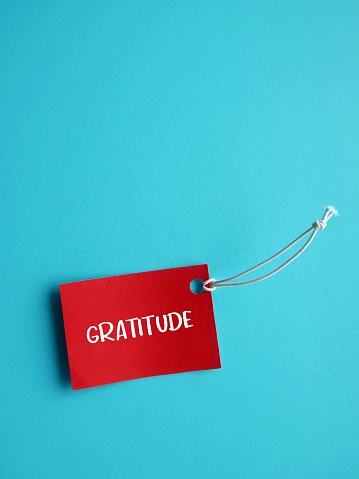 Red paper tag on blue copy space background with handwritten text GRATITUDE, feeling thankful for good things in life. taking moment to reflect on how lucky you are