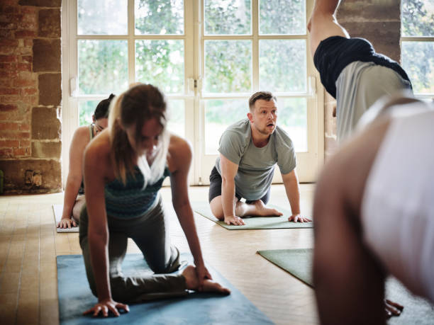 istock Yoga, class and people stretching in exercise, workout or training on mat for health and wellness. Fitness, gym or group on floor in pilates and movement of body for self care and flexibility 1805720571