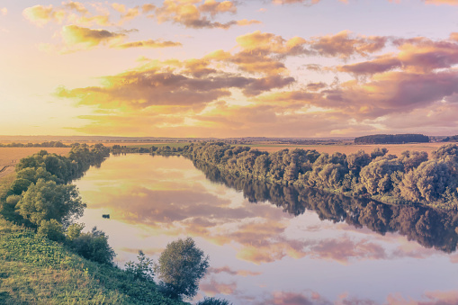 A sunset or sunrise scene over a lake or river with cloudy skies reflecting in the water on a summer evening or morning. Landscape. Aesthetics of vintage film.
