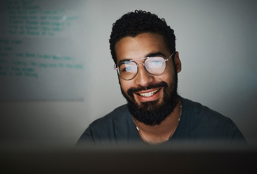 A happy entrepreneur working late into the night while sitting at his desktop computer. Stock photo