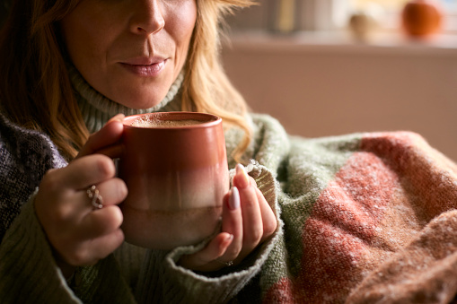 Close Up Of Woman At Home Wearing Winter Jumper With Warming Hot Drink Of Coffee In Cup Or Mug