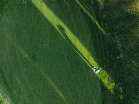 Aerial view of a golfer putting on green. Man's shadow between trees.