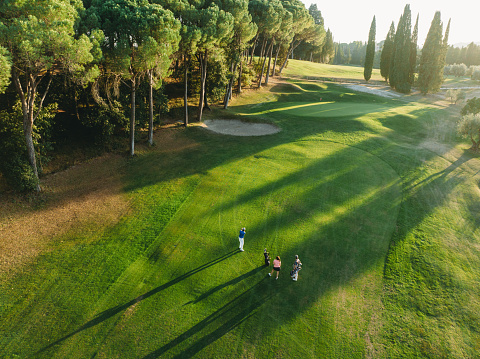 Aerial view of three people golfing together. They are standing on the golf course at sunset.