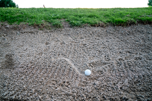The golfer comes out of the bunker by hitting the ball with a golf club, on a winter day with wet grass.