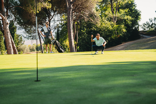 A golf player is reading the green. He's playing golf on the course.