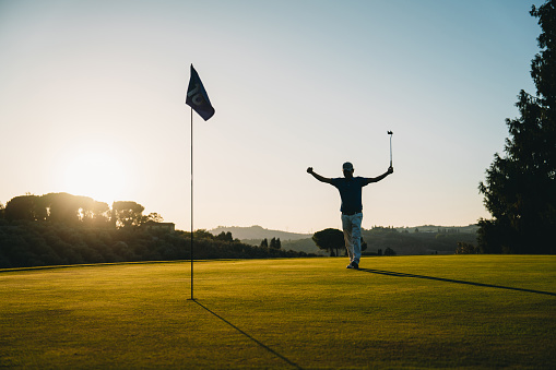 A golfer is celebrating a hole at sunset on the green. Silhouette style image with copy space.